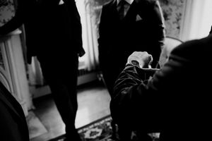 Black and white photo of groomsmen preparing, with one adjusting another's cufflinks before a wedding ceremony.
