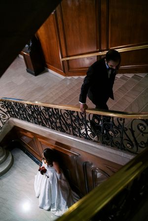 Bride and groom descend an elegant staircase with ornate iron railings in a grand venue during their wedding.
