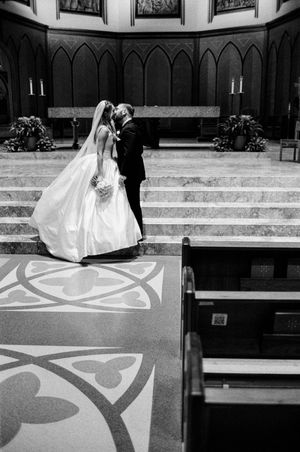 Black and white photo of bride and groom sharing first kiss at church altar during wedding ceremony.