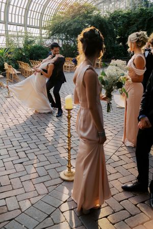 Bride and groom share a romantic dance at an indoor greenhouse wedding ceremony with bridesmaids in blush gowns.