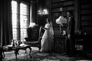 Black and white photo of bride and groom in elegant library with ornate furniture and bookshelves.