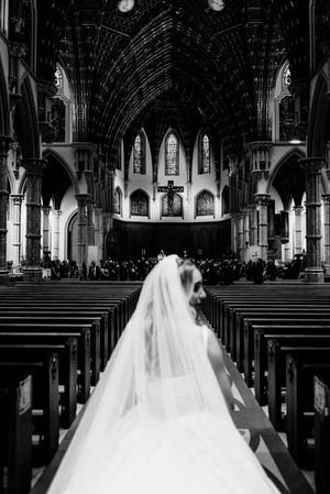 Black and white photo of a bride walking down the aisle of a grand Gothic cathedral on her wedding day.
