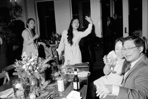 Black and white photo of guests at a dinner party table with floral centerpieces and bottles.
