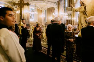 Elegant wedding ceremony inside ornate Catholic church with guests and altar servers standing near golden statues.
