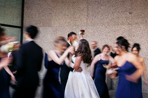 Bride and groom share a kiss surrounded by bridesmaids in navy dresses at an outdoor wedding celebration.