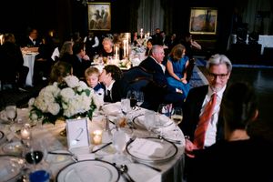 Elegant formal dinner reception with guests seated at candlelit tables adorned with white floral centerpieces in a grand hall.