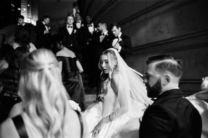 Black and white wedding photo of bride in veil descending grand staircase with groom and wedding party.