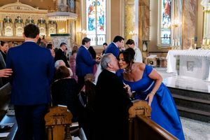 Guests in formal attire greet each other inside an ornate Catholic church during a wedding ceremony.