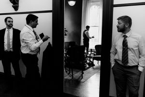 Black and white photo of groomsmen in dress shirts and ties preparing before a wedding ceremony.
