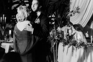 Black and white photo of couples dancing and sitting at a decorated table during an elegant wedding reception.
