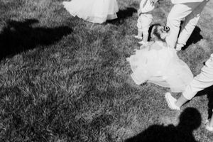 Black and white photo of children in formal wedding attire playing on grass with shadows visible.