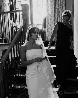 Black and white photo of a bride in a strapless gown and lace veil descending a staircase.