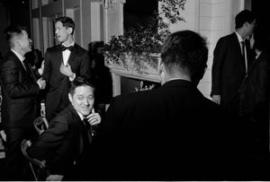 Black and white photo of elegantly dressed wedding guests socializing outdoors at a formal evening reception.