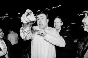 Black and white photo of excited man pointing at camera at a lively party event.
