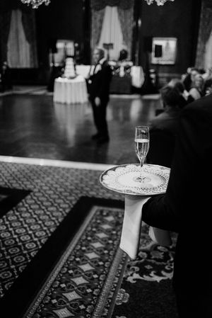 Black and white photo of champagne flute on ornate tray at elegant wedding reception in grand ballroom.