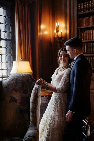 Bride in lace gown and groom in navy suit share a tender moment in an elegant wood-paneled library with warm lighting.