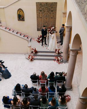 Aerial view of an elegant wedding ceremony with guests seated in rows, couple at altar adorned with red floral arrangements.