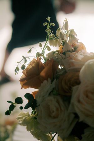 Close-up of an elegant wedding bouquet featuring peach roses, white blooms, and delicate greenery in soft natural light.