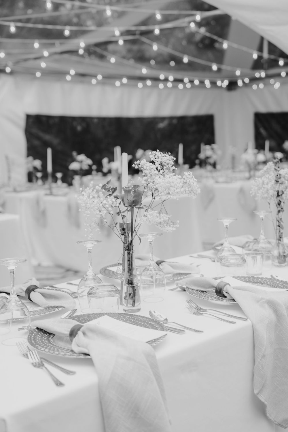 Elegant black and white wedding reception table setting with floral centerpieces, candles, and string lights overhead.