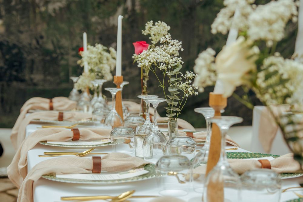 Elegant outdoor wedding table setting with white florals, candles, gold cutlery, and blush linens.