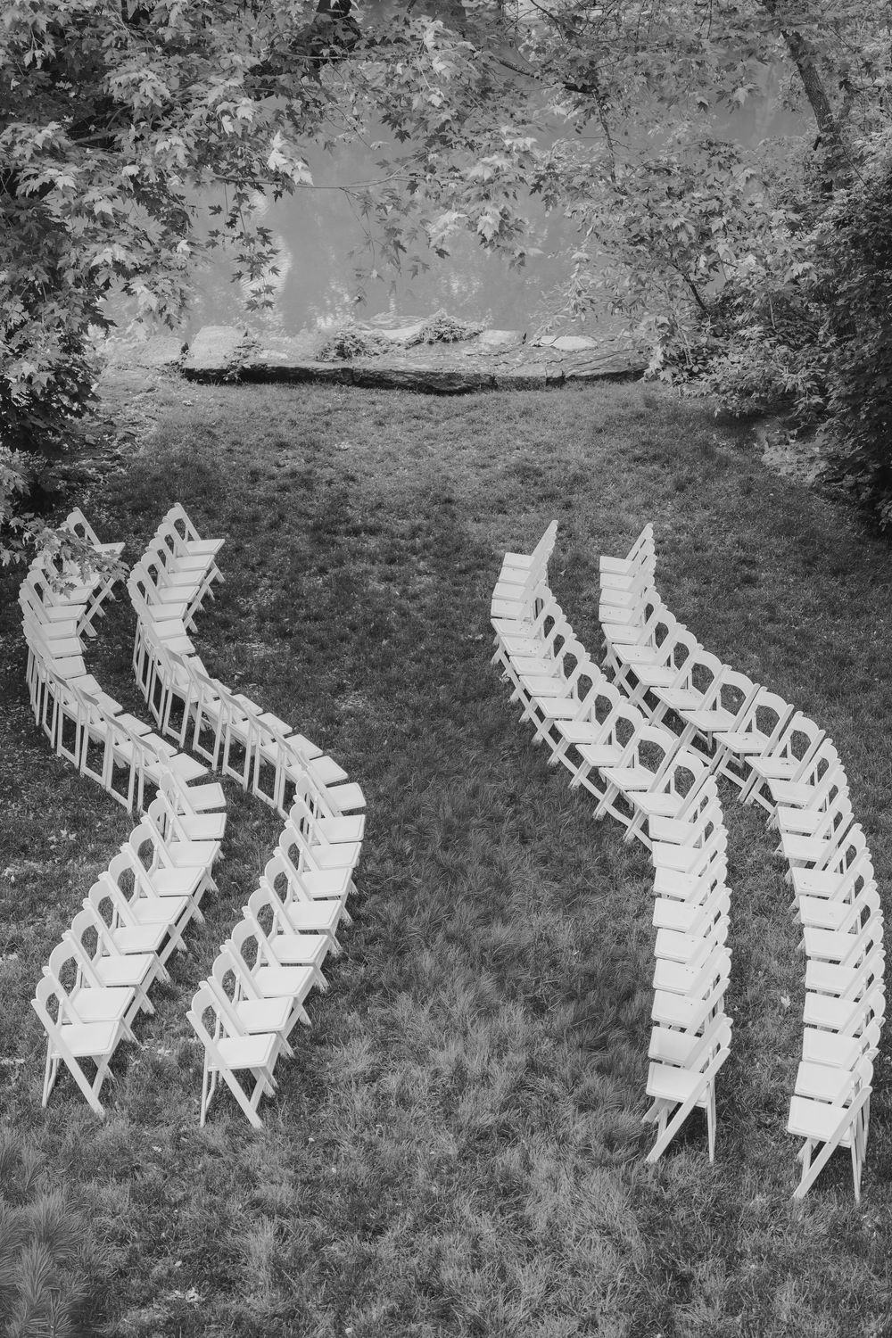Black and white aerial view of curved rows of white folding chairs set up on grass for an outdoor wedding ceremony.
