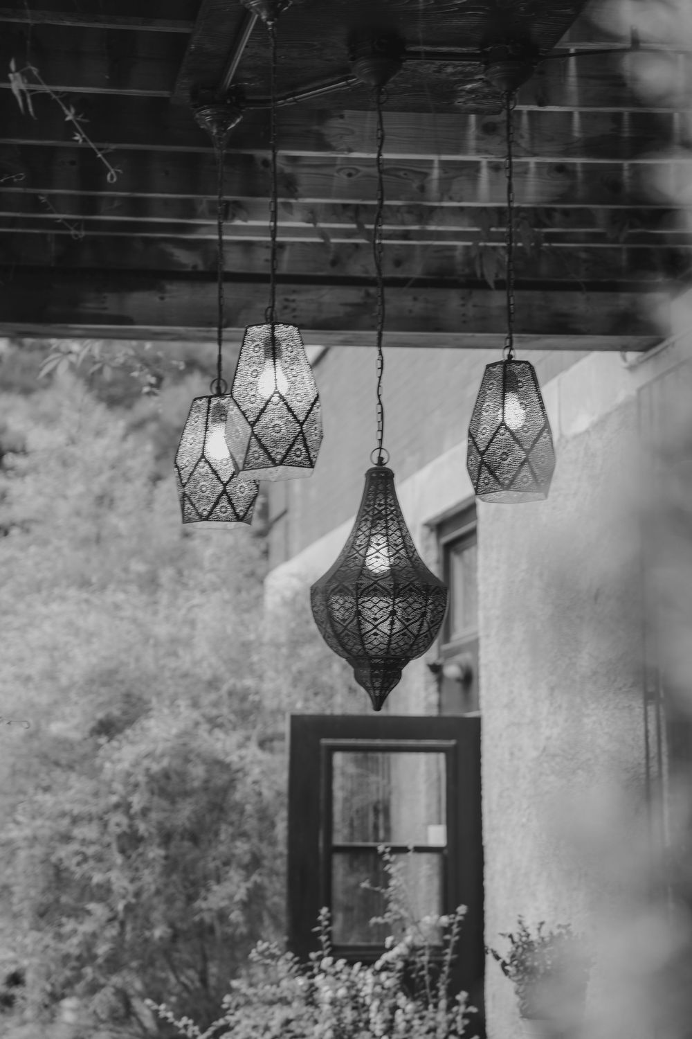 Ornate Moroccan-style hanging lanterns with intricate filigree patterns suspended from a wooden beam outdoors.