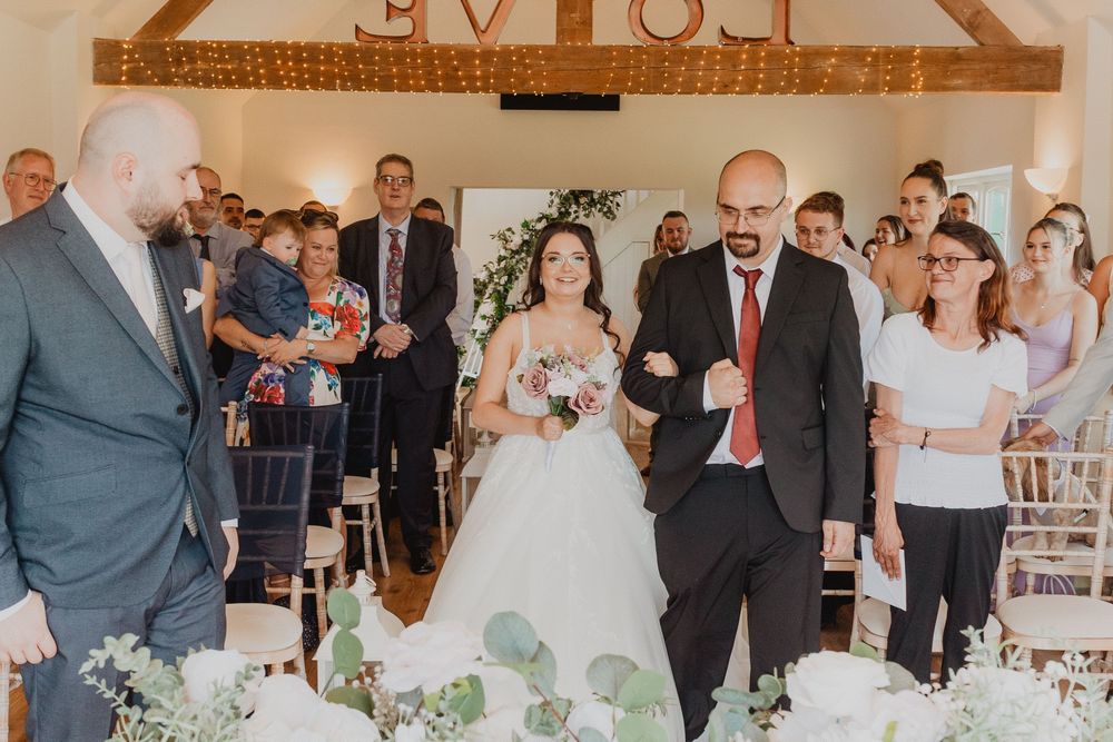 Bride and groom walk down the aisle together in a rustic barn wedding venue decorated with greenery and fairy lights.