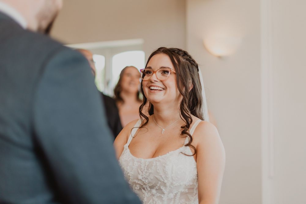 Radiant bride in lace gown smiling joyfully during wedding ceremony.