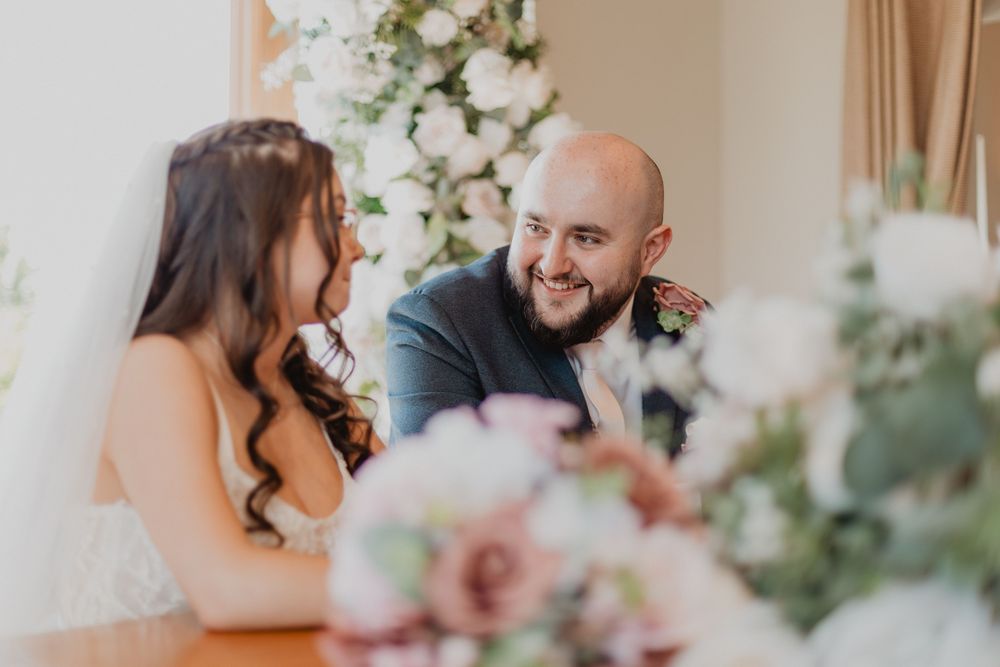 Bride and groom share a joyful moment at the wedding ceremony table, surrounded by elegant floral arrangements.