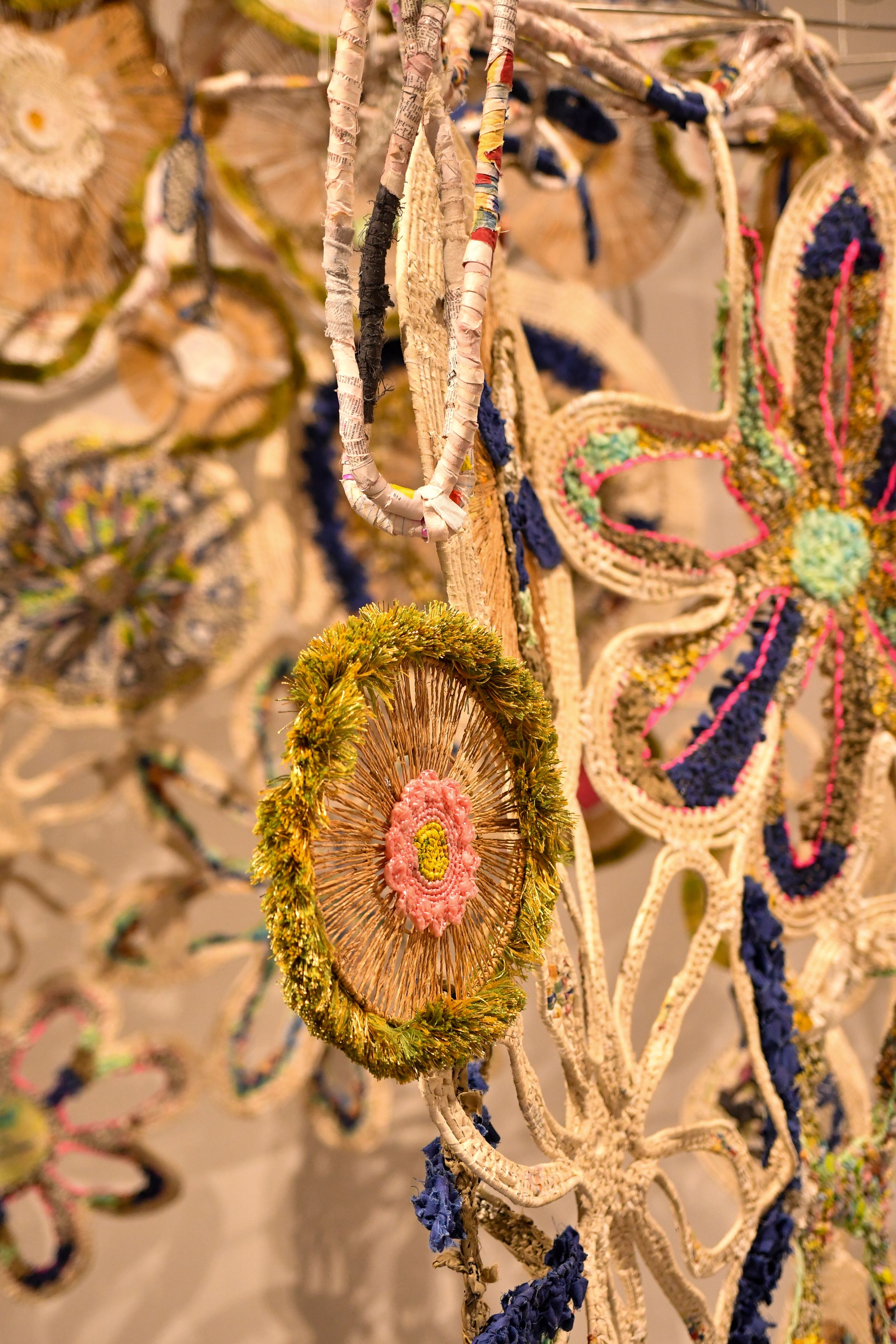 Colorful handmade crocheted floral decorations with beads and yarn in cream, yellow, pink, and blue tones hanging as wall art.