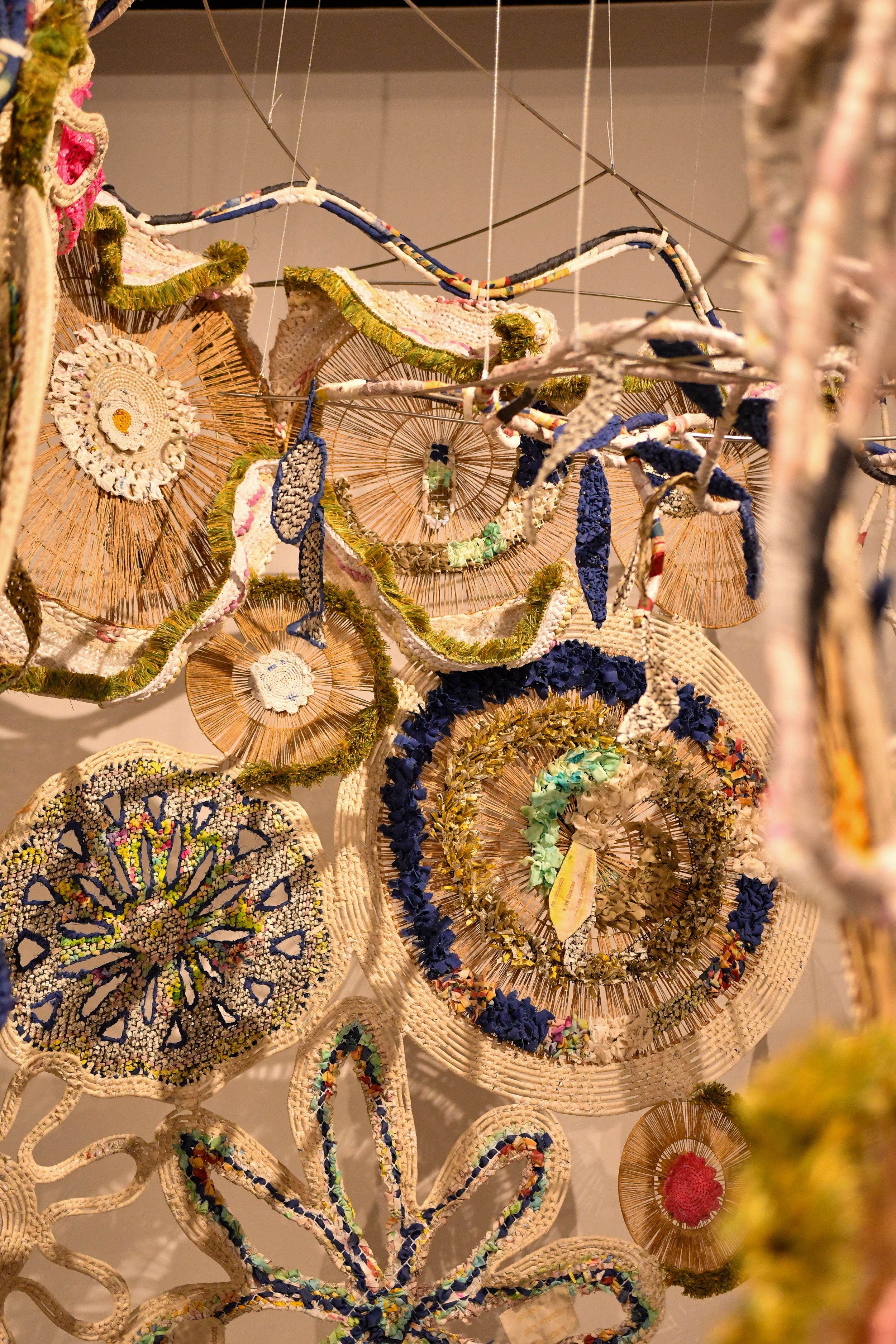 Colorful handmade textile art installation with woven circular shapes, beads, and fringe hanging from strings.