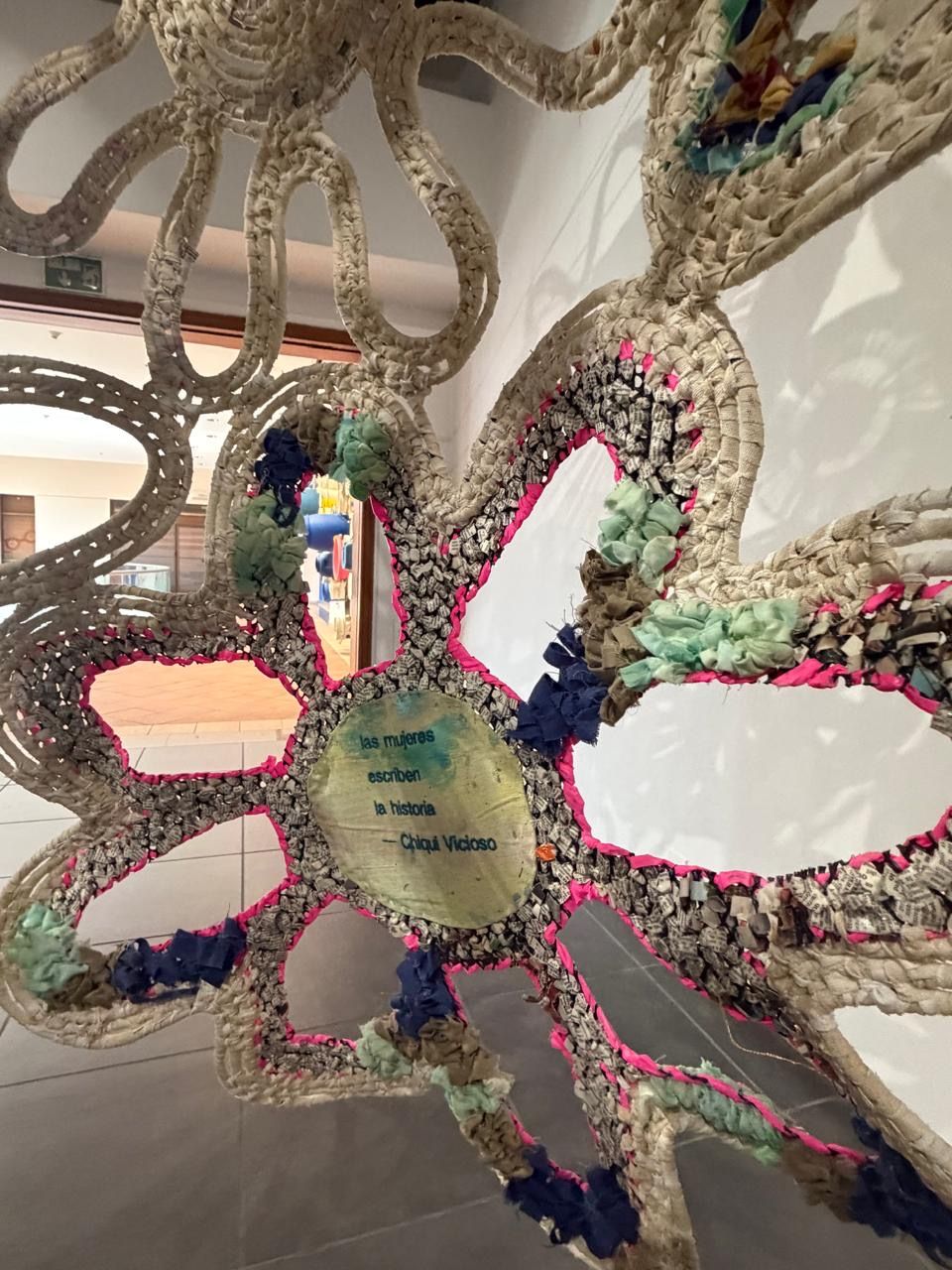 Colorful crocheted textile art installation with pink, teal, and navy accents displayed in a gallery setting.