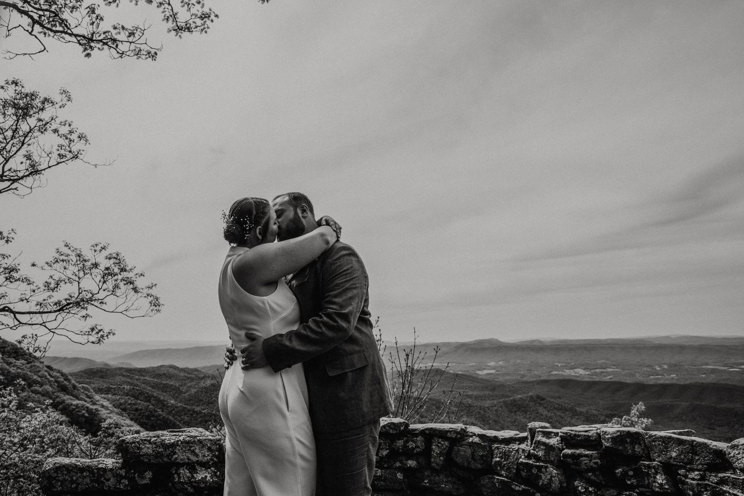 Black and white photo of newlywed couple embracing with a scenic mountain valley backdrop.