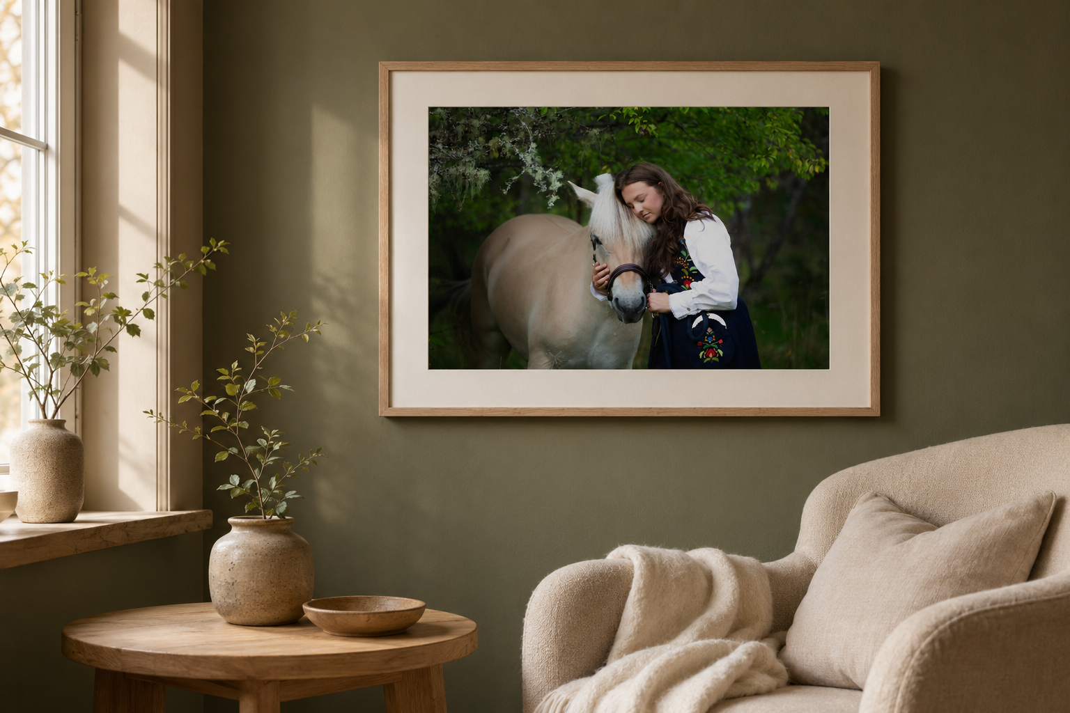 Framed photo of a woman with a white horse displayed on a sage green wall above a beige armchair in a cozy living room.