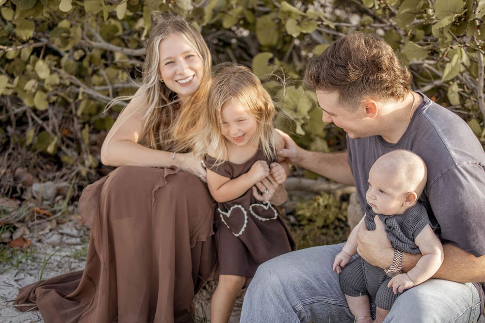 Happy family with two children smiling outdoors near lush green plants on a sunny day at the beach.