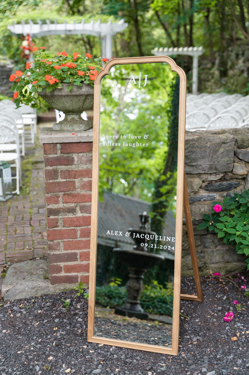 Gold-framed wedding welcome mirror sign for Alex & Jacqueline dated 09.21.2024, displayed outdoors at elegant garden venue.