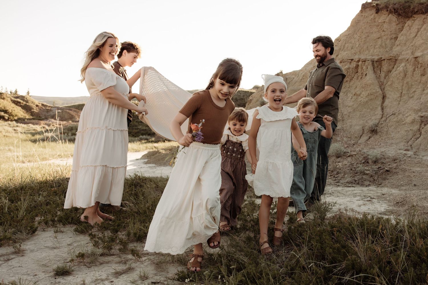 Family photo session in golden hour light with parents and four children playing in a sandy landscape.