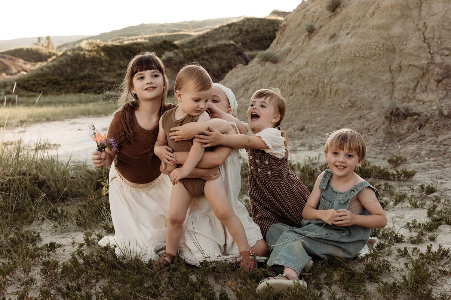 Four young children sitting together outdoors in earthy toned outfits while being photographed for a family shoot