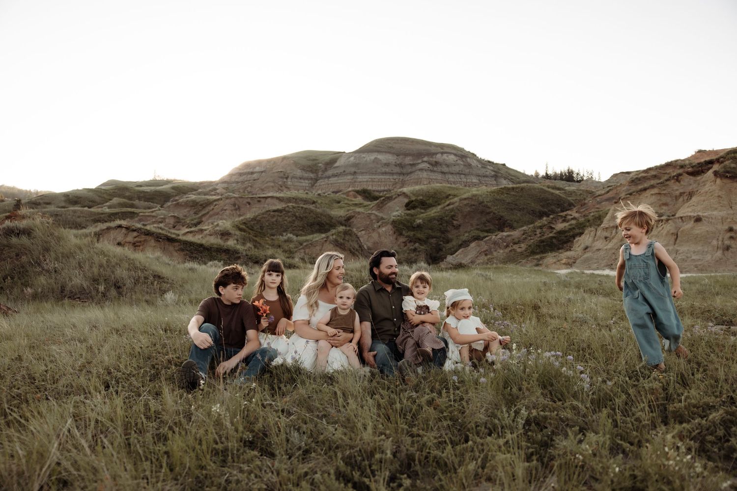 Family with children relaxing in lush green badlands grass at dusk doing a Central Alberta photoshoot