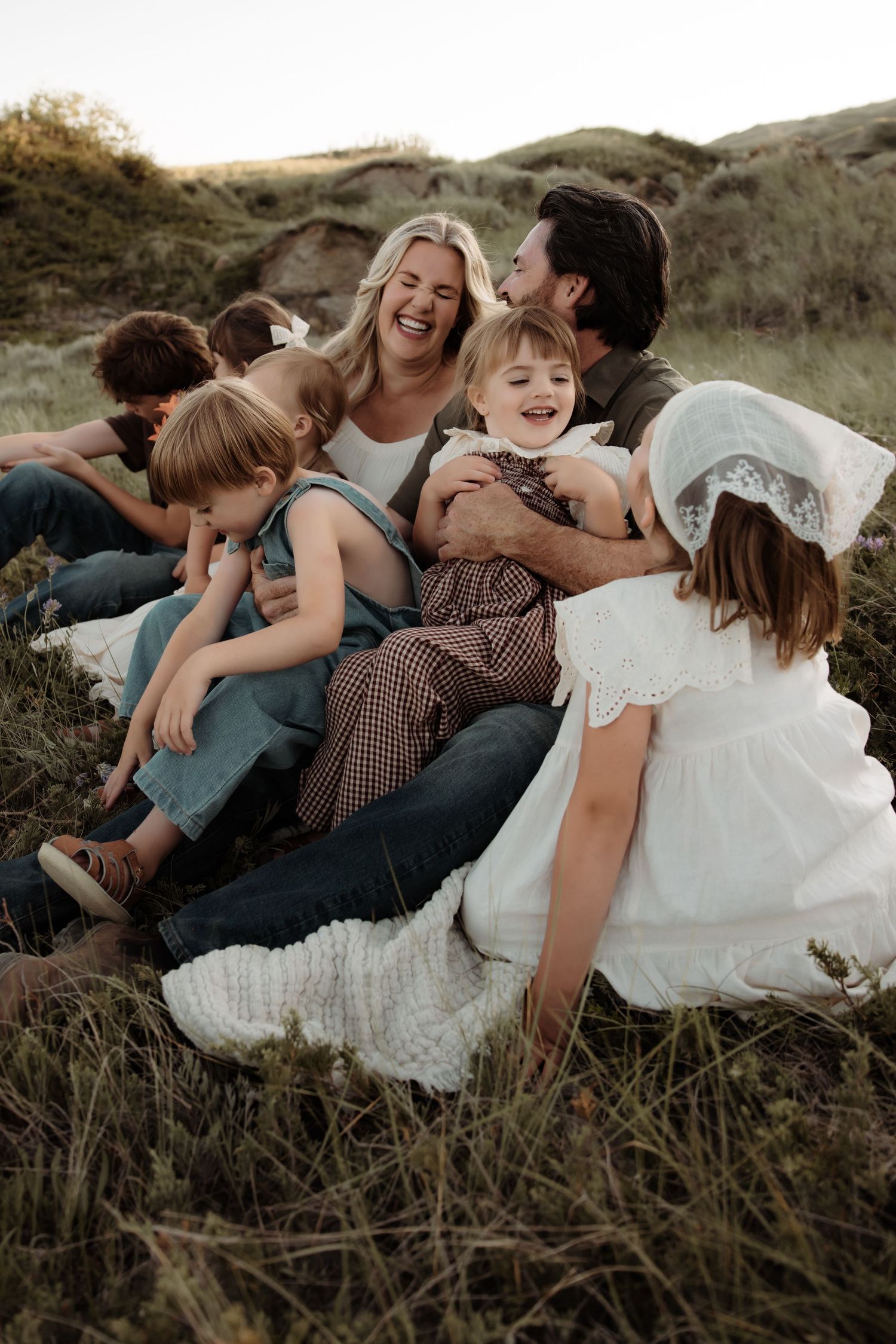 A family laughs together outdoors in a grassy field, with parents and children a, candid moment during their red deer photography shoot