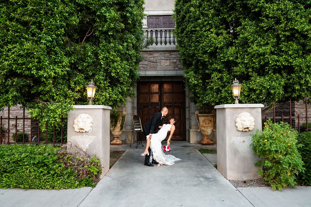 Bride and groom share a romantic dip pose at an ivy-covered mansion entrance with stone pillars and lanterns.