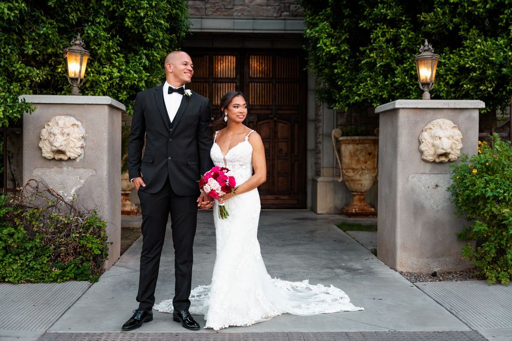 Bride and groom posing in front of elegant wooden doors with lion sculptures and lanterns at outdoor wedding venue.