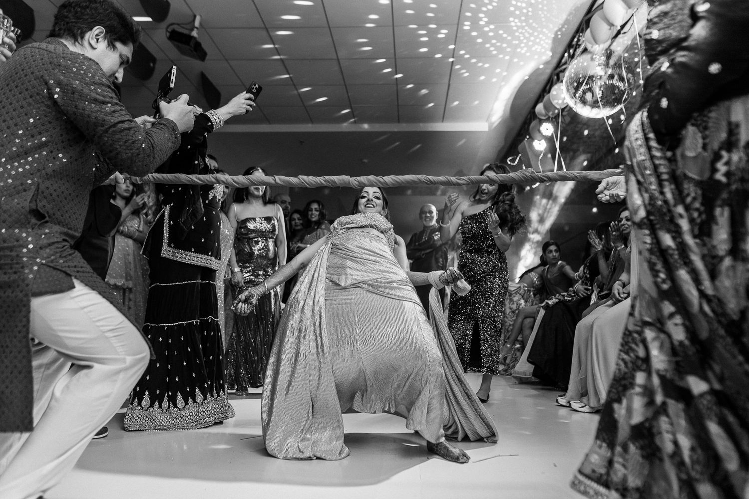 Black and white wedding photo of couple sharing first dance surrounded by guests at elegant reception venue.