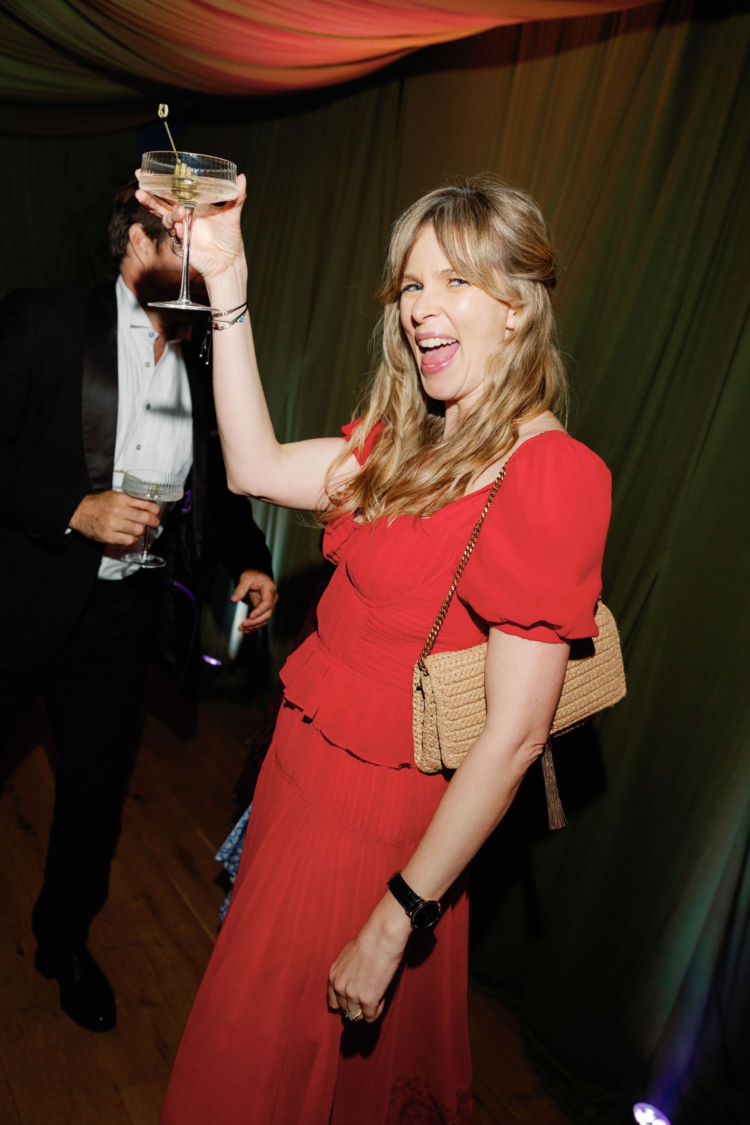 Woman in red dress raises cocktail glass at elegant party event.