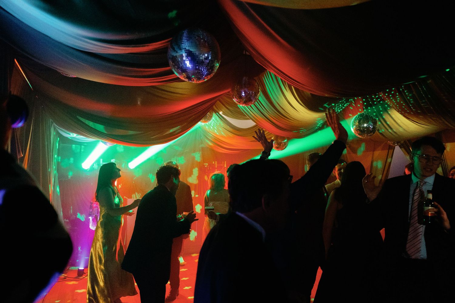 People dancing under colorful lights and disco balls at a festive party or wedding reception.