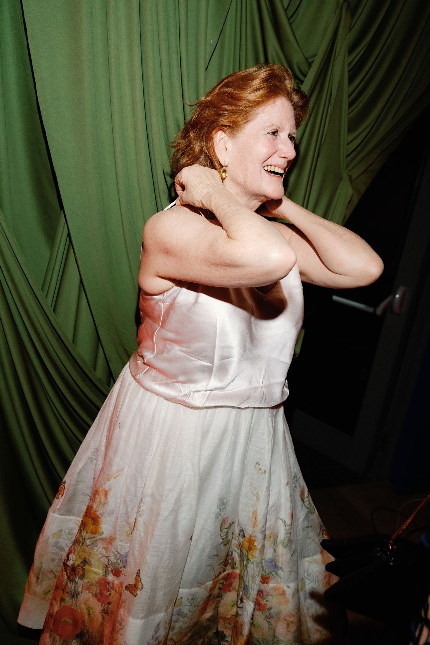 Woman in floral dress laughs joyfully while dancing at a wedding reception.