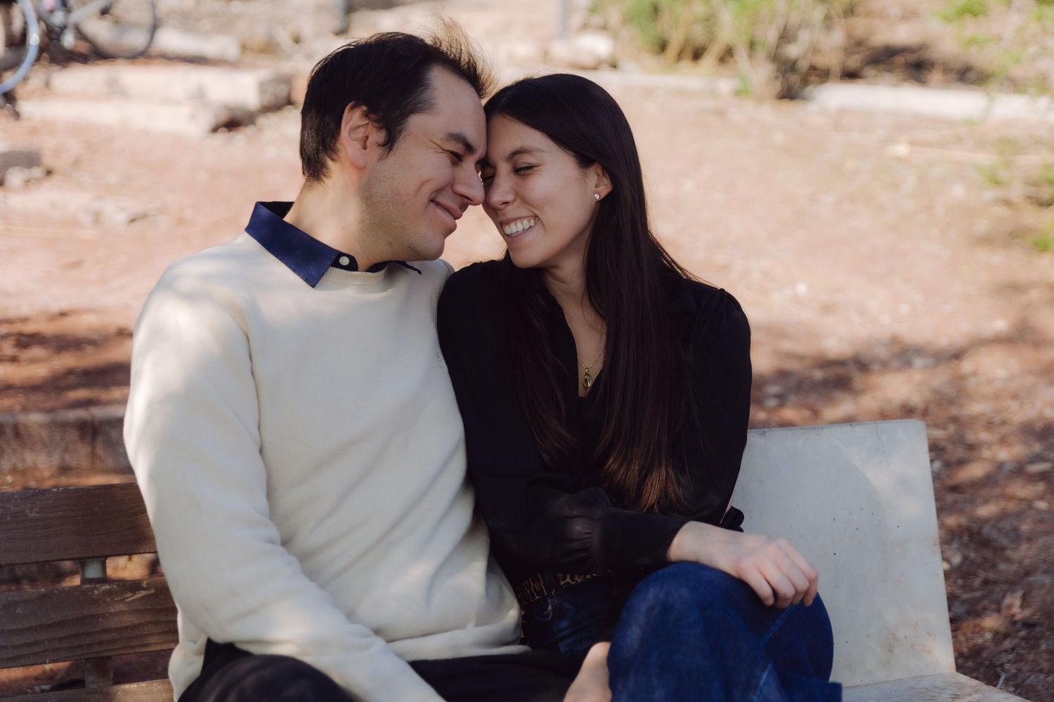 Romantic couple sitting close on a bench, smiling and touching foreheads outdoors.