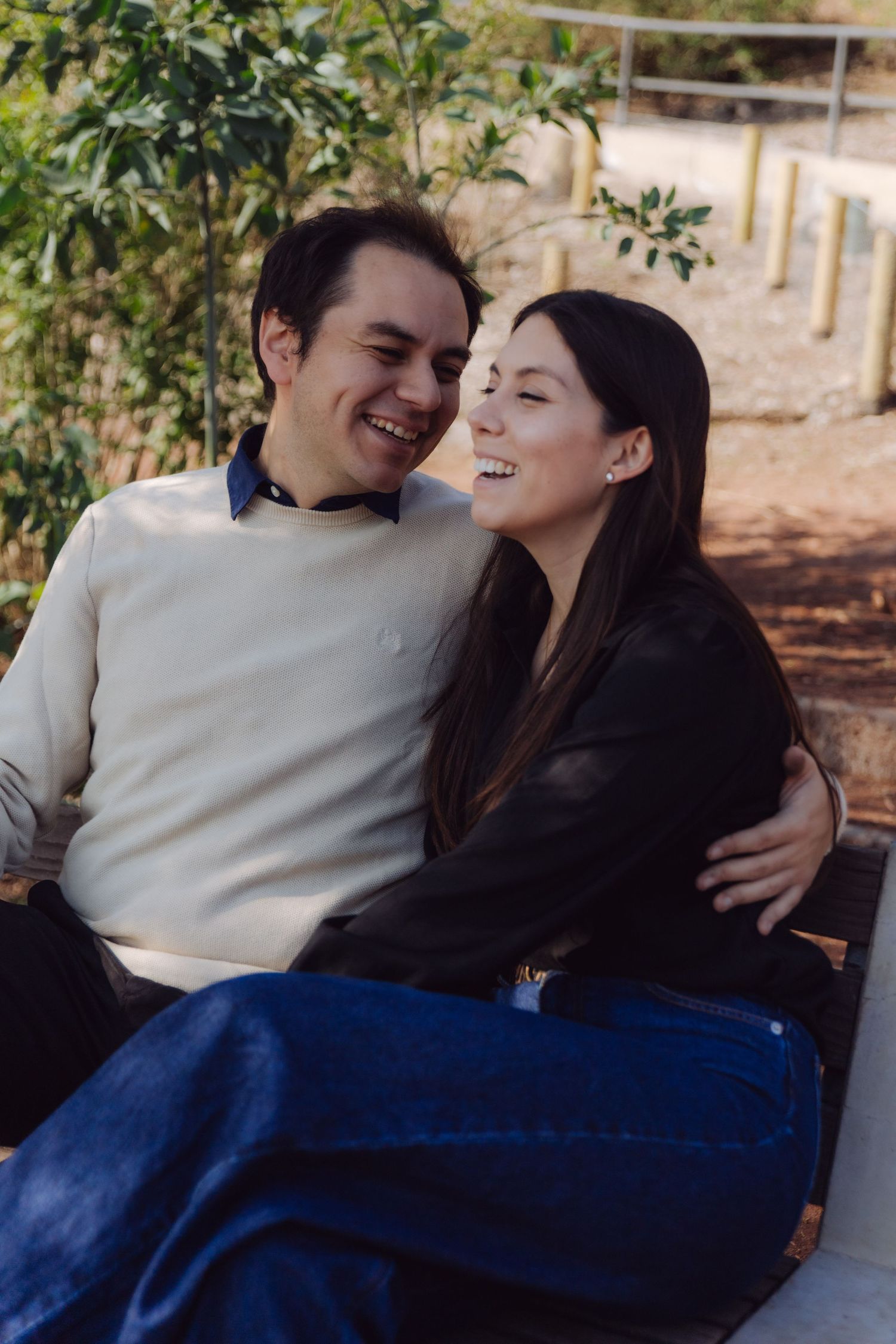 Smiling couple embracing warmly on a bench surrounded by lush greenery in a sunny park.