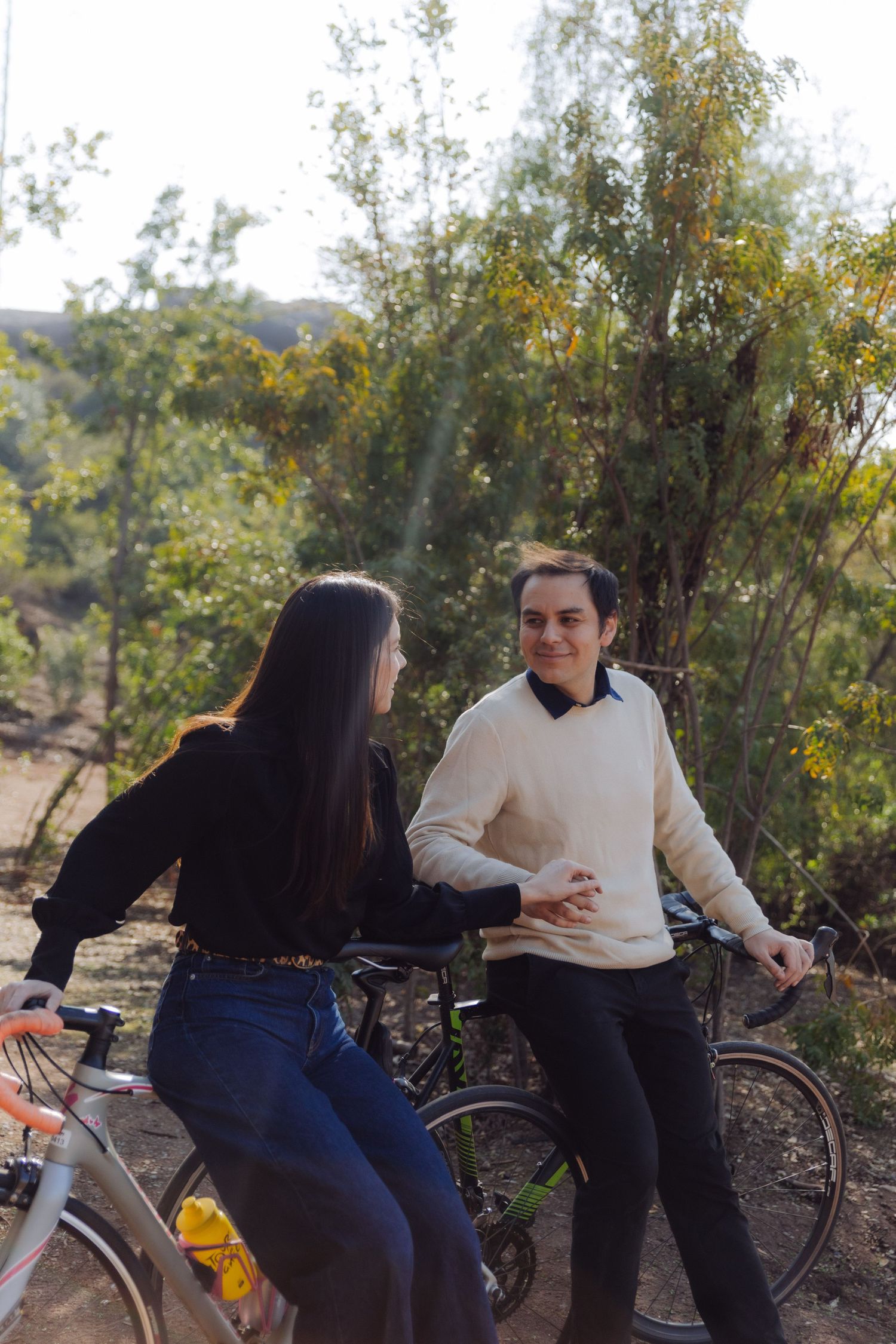 Couple with bicycles talking in a sunny park surrounded by green trees.