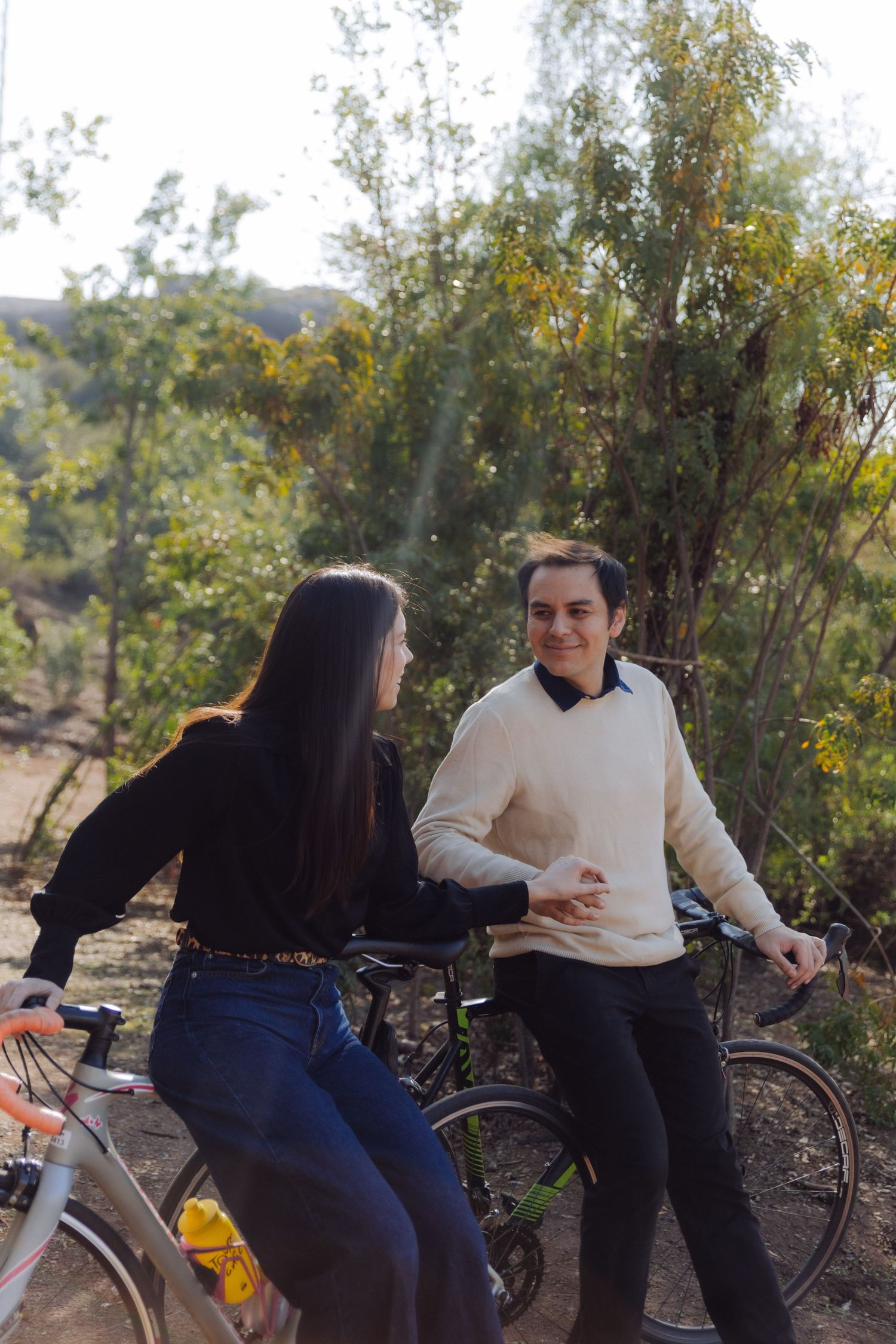 Two people smiling and chatting beside their bikes in a lush outdoor setting.